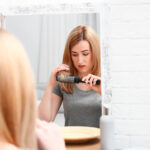 Emotional woman brushing hair near mirror in bathroom