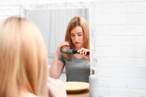 Emotional woman brushing hair near mirror in bathroom
