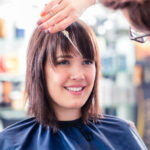 Hairdresser cutting woman hair in shop